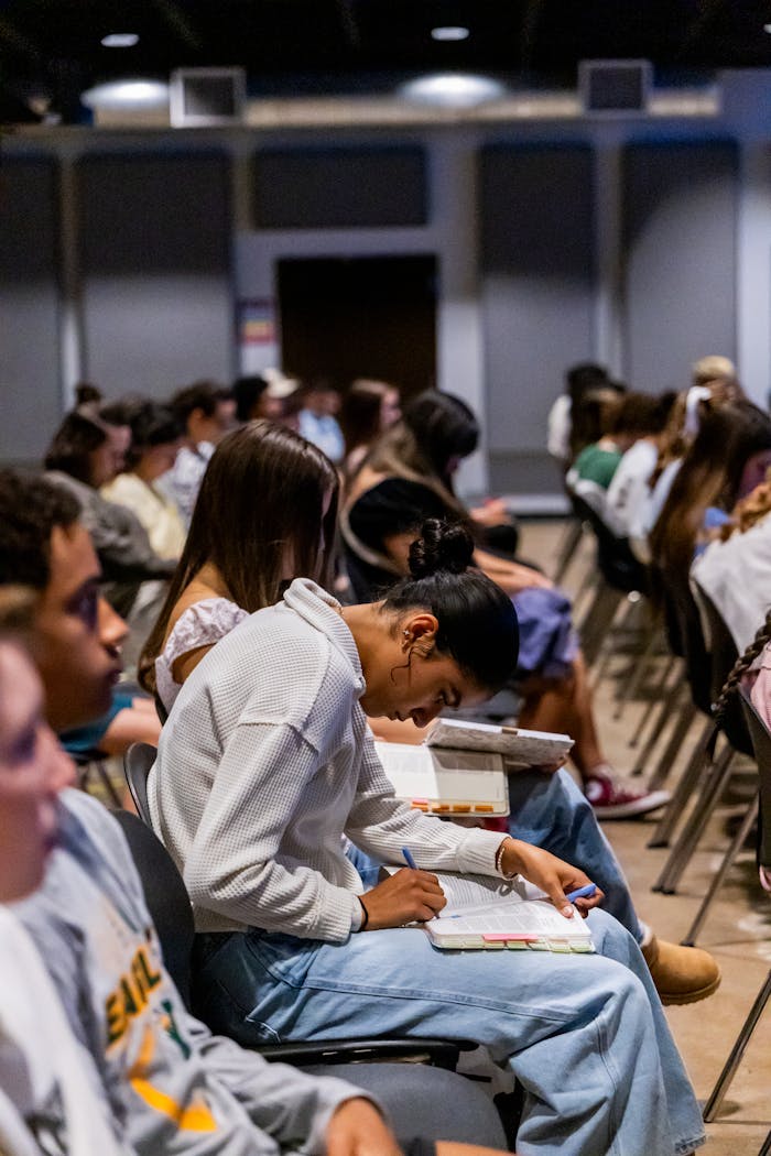 Students attentively taking notes during a classroom lecture setting indoors.